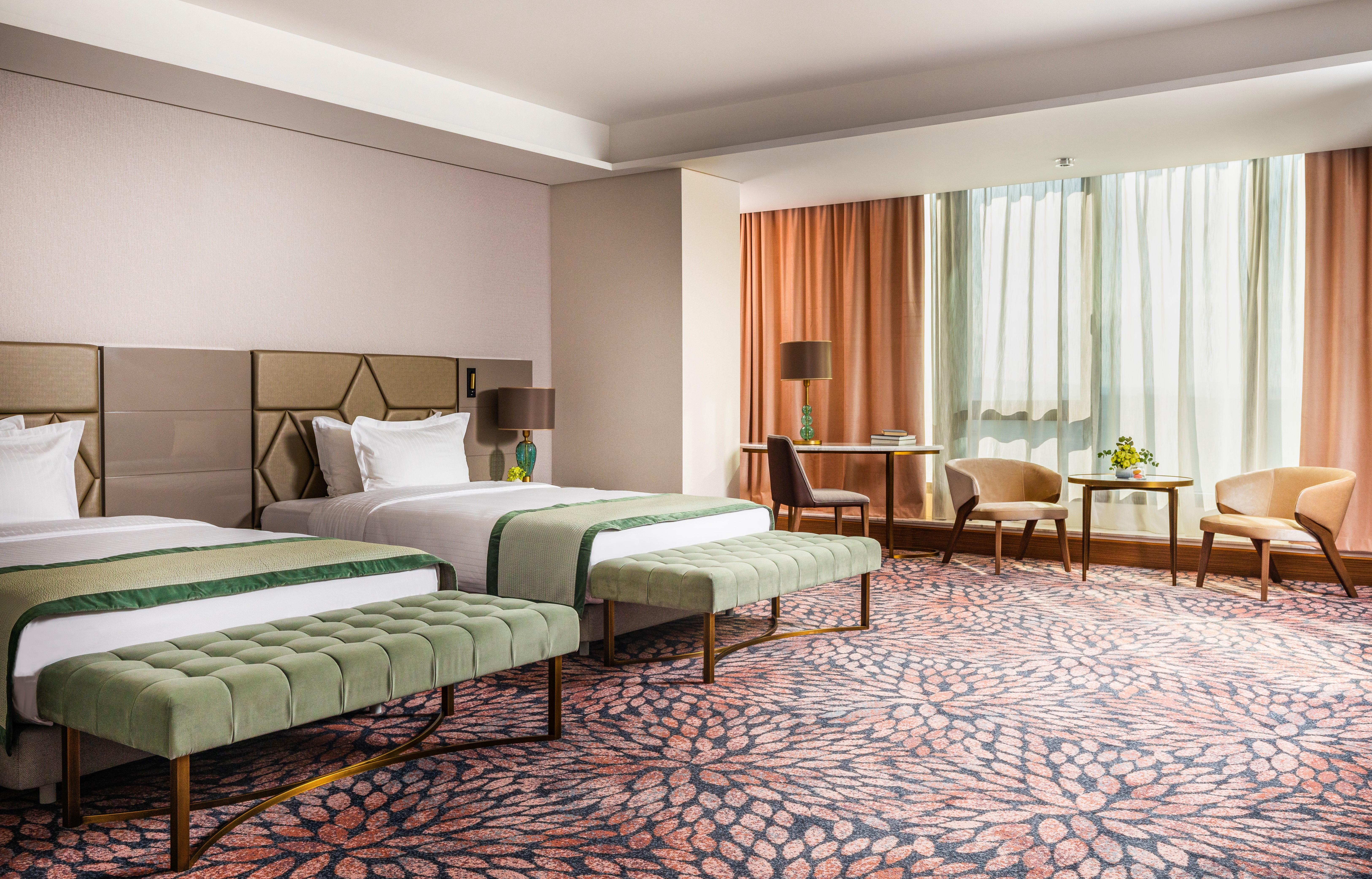 Grand Hotel Millennium Sófia Exterior foto The image shows a well-decorated hotel room featuring two beds with green striped bedspreads. There is a plush green bench at the foot of each bed. The room has large windows with sheer curtains allowing natural light to enter. There is a cozy seatin