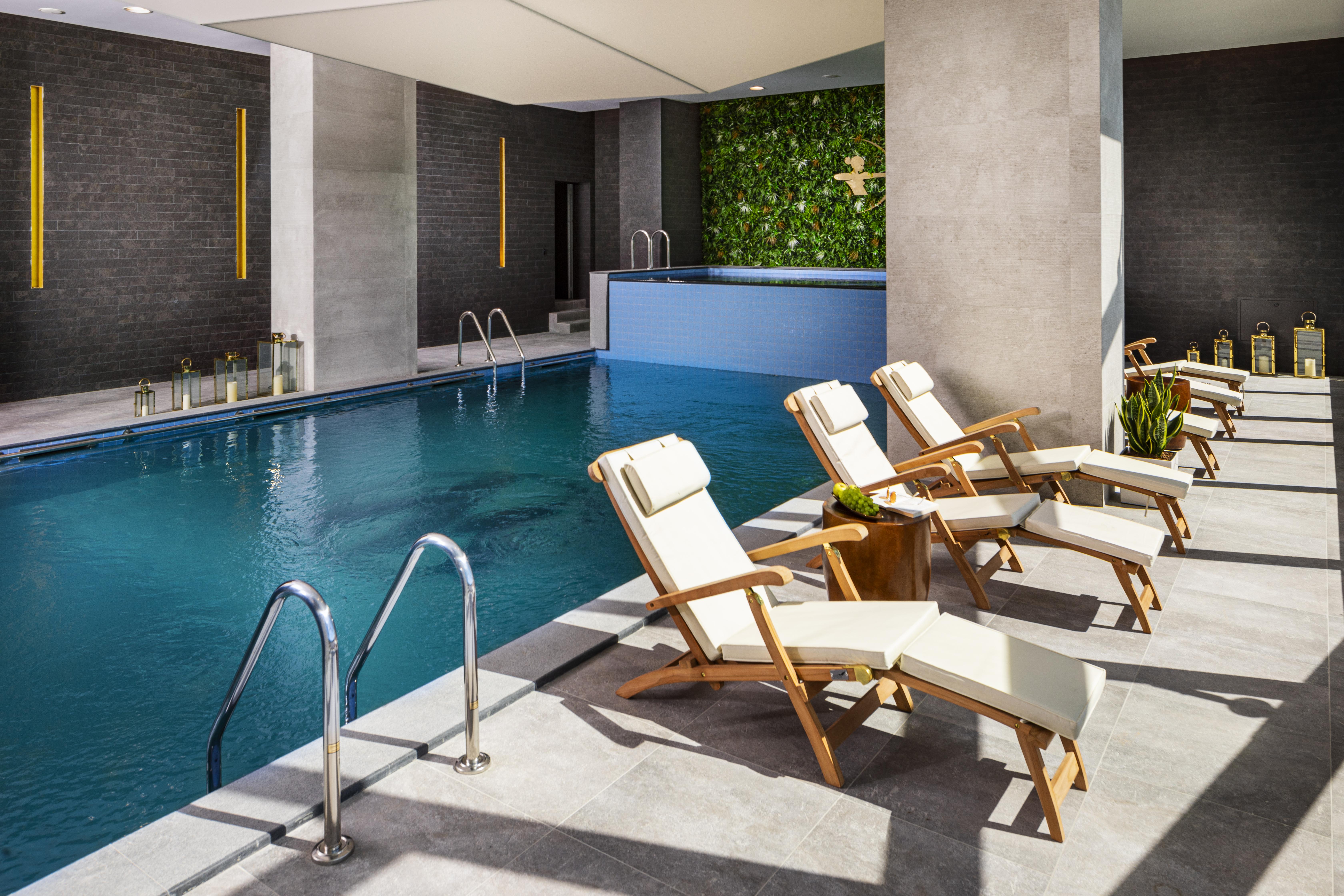 Grand Hotel Millennium Sófia Exterior foto The photo shows a serene indoor swimming pool area. The pool is clear and inviting, with a blue water surface reflecting light. Along one side of the pool, there are several light-colored lounge chairs with white cushions, positioned for relaxation. 